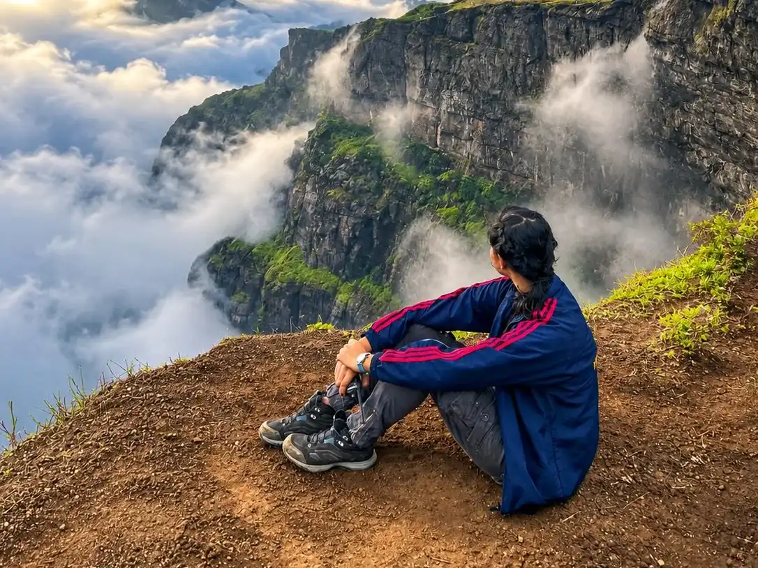A trekker resting on a rock above a green valley